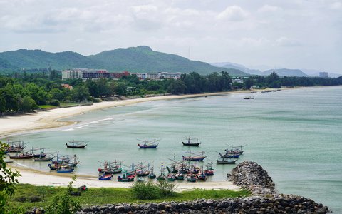 Fishing boats moored in the bay at Khao Tao beach near Hua Hin, with green hills behind