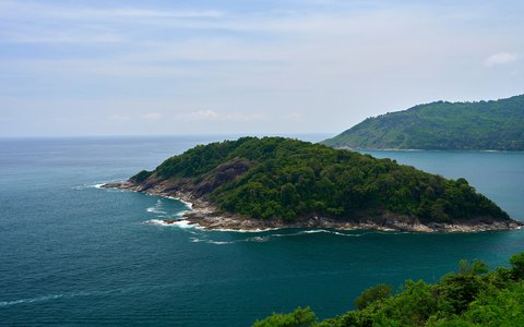 A green wooded island in a sparkling blue sea off the coast at Kamala, under a pale blue sky