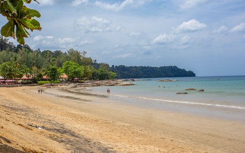 A quiet sandy beach curving round a bay at Khao Lak, with palm trees, green hills and a blue sky with clouds