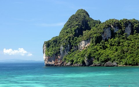 A limestone cliff covered in green jungle rising from turquoise water at Ao Nang, under a blue sky