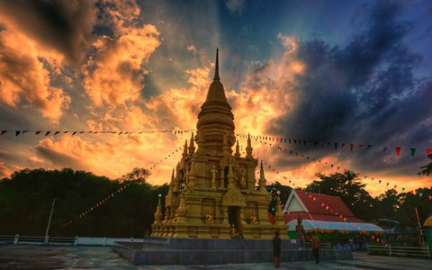 A golden pagoda with prayer flags under an orange and dark cloudy sky