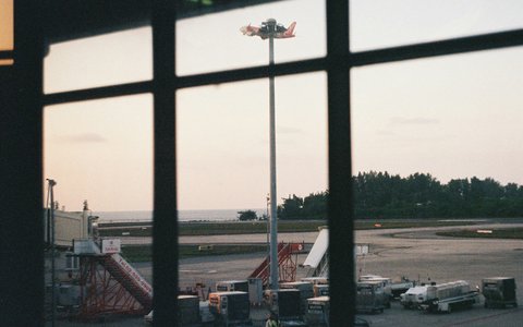 The apron at Phuket Airport with boarding stairs and ground vehicles, seen through a terminal window