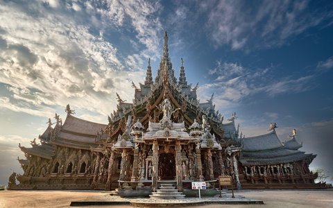 A large carved wooden temple building with tall spires under a blue sky with white cloud