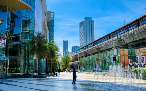 Glass frontage of Siam Paragon beside the elevated skytrain line and a fountain plaza in Bangkok