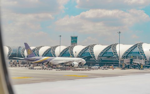 Thai Airways airliner on the apron in front of the curved terminal roof and control tower at Suvarnabhumi Airport