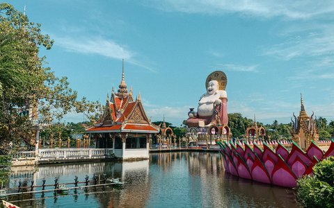 Temple pavilion, lotus-shaped boat and a large Happy Buddha statue beside the lake at Wat Plai Laem on Koh Samui