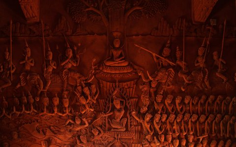 A red carved wall relief of a seated Buddha surrounded by rows of figures