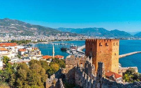 The red octagonal Kizil Kule tower above Alanya harbour, with the town, the sea and mountains under a blue sky
