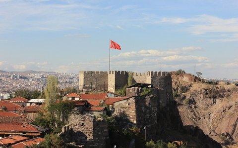 Alte steinerne Burgmauern mit türkischer Flagge über rot gedeckten Häusern und Felsen in Ankara
