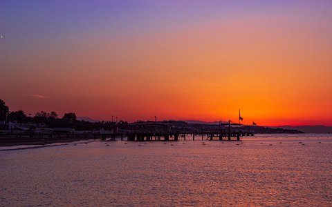 A long pier silhouetted against an orange and pink sunset sky over the sea at Belek