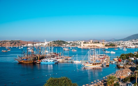 Gulets and sailboats in Bodrum marina with Bodrum Castle across the bay, under a bright blue sky