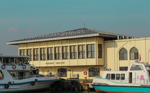 The historic Kadikoy ferry pier building with ferries moored alongside, under a blue sky