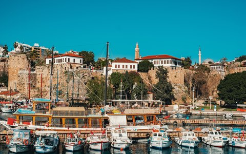 Boats moored in the old harbour of Kaleici below the walls and red-roofed houses of Antalya's old town, under a blue sky