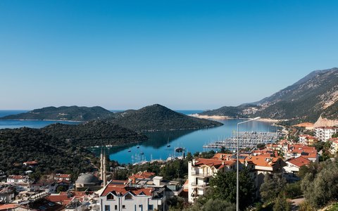 Aerial view of Kas harbour and white houses with green hills and blue sea under a clear sky