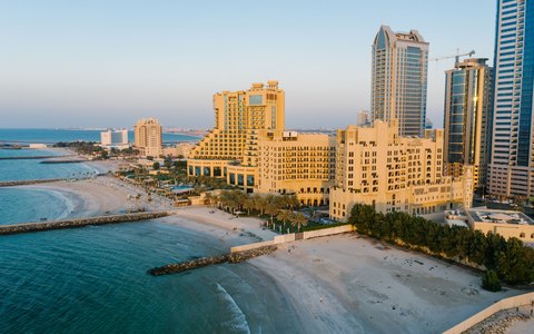 Aerial view of Ajman's beach and seafront hotels and towers beside calm water in late afternoon light