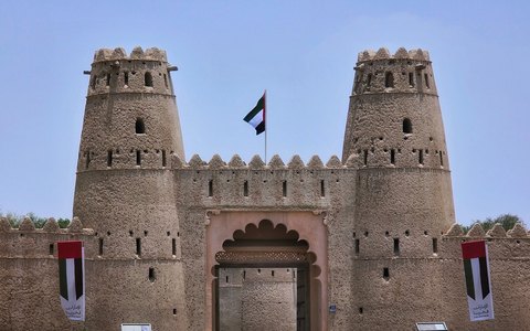 The twin round towers and gateway of Al Jahili Fort with the UAE flag, under a clear blue sky