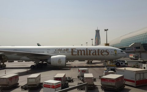 Emirates-Flugzeug auf dem Vorfeld am Flughafen Dubai, davor Frachtcontainer, dahinter das Terminal