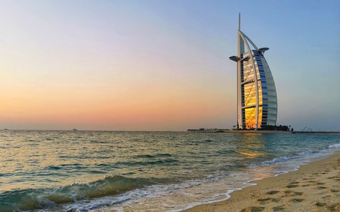 The sail-shaped Burj Al Arab beside the sea, seen from Jumeirah Beach with small waves and a sunset sky