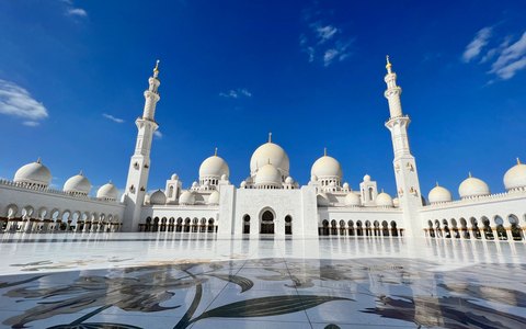 The white domes and tall minarets of the Sheikh Zayed Grand Mosque under a clear deep blue sky