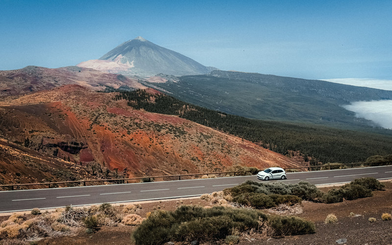 Der Teide über roten Vulkanhängen mit einem Auto auf der Straße darunter